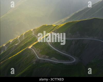 Aerial view of a serpentine road winding through verdant mountains under a soft, golden sunlight, Alazani pass, Chala, Kakheti, Georgia. Stockfoto
