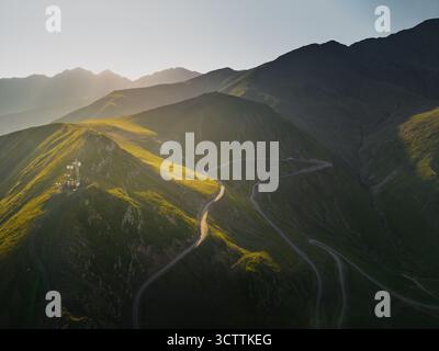 Aerial view of a winding mountain road bathed in golden sunlight cuts through verdant hillsides, leading to a distant peak, Chala, Kakheti, Georgia. Stockfoto