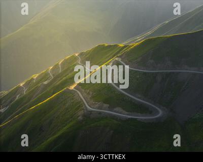 Aerial view of a winding road snaking across verdant hillsides, kissed by golden light at Alazani pass, Chala, Kakheti, Georgia. Stockfoto