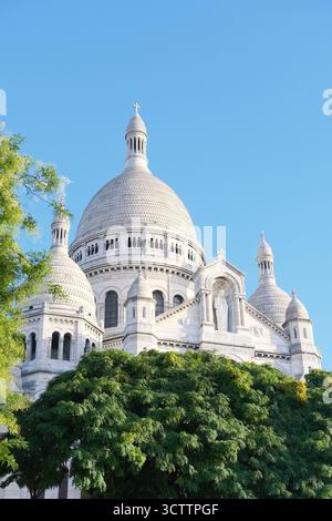 Basilika des Heiligen Herzens von Montmartre, Basilika Sacré-Cœur in Paris, Frankreich, grüne Bäume vor blauem, klarem Himmel. Reisen, Urlaub in Europa Stockfoto