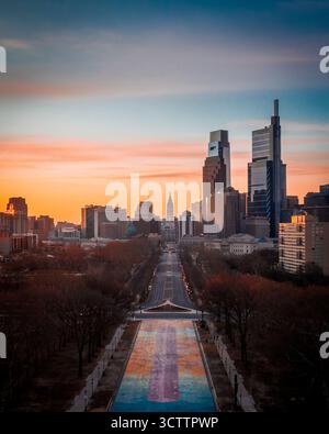 Der Logan Square aus der Vogelperspektive spiegelt den lebhaften Sonnenaufgang wider, während er sich in Richtung Philadelphias Skyline mit dem Rathaus und den modernen Wolkenkratzern in Philadelphia, Pennsylvania, USA erstreckt. Stockfoto