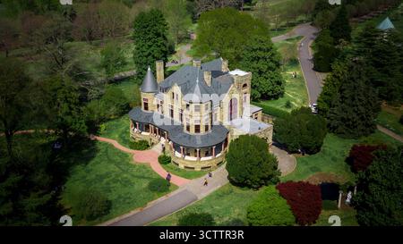 Blick aus der Vogelperspektive auf ein großes, historisches Gebäude mit Türmchen und einer umlaufenden Veranda, eingebettet zwischen grünen Bäumen und gewundenen Pfaden, Richmond, Virginia, USA. Stockfoto