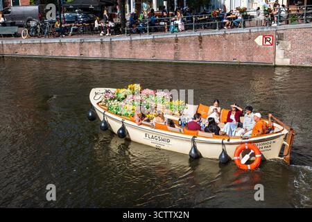Amsterdam, Niederlande, 29. August 2025. Menschen an Bord des Flagship-Kanalbootes, dekoriert mit bunten Blumentöpfen. Top-Down, Weitwinkelüberblick Stockfoto