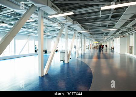 Flughafen Schiphol, Amsterdam, Niederlande, 29. August 2025. Terminal Verbindungsgang oder Korridor mit großen Fenstern und Passagieren, die Gepäck ziehen Stockfoto