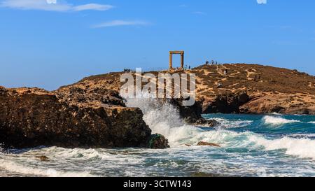 Brechende Wellen krachen gegen dunkle Felsen vor der riesigen Portara, einem antiken griechischen Denkmal eines Tempels für apollo auf naxos Stockfoto
