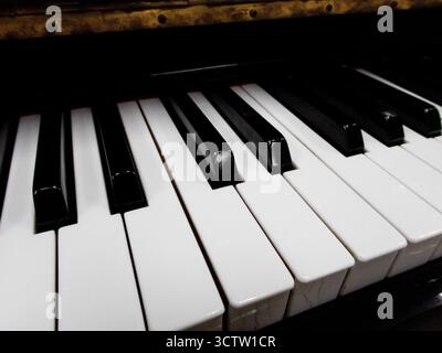 Enge Seitenansicht der glänzenden schwarz-weißen Klaviertasten mit der Reflexion der goldenen Messingkante aus niedrigem Winkel mit geringer Schärfentiefe. Stockfoto
