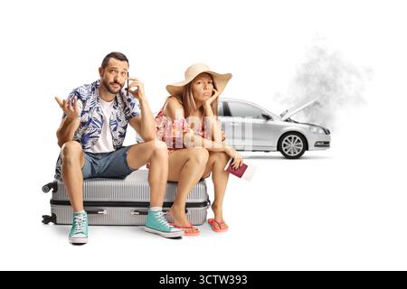 Ein junges Paar, das auf einem Koffer sitzt und den Pannendienst wegen Pannenproblemen anruft, isoliert auf weißem Hintergrund Stockfoto