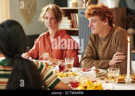 Gruppe junger Erwachsener Freunde, die Thanksgiving-Mahlzeit genießen und sich am Tisch unterhalten Stockfoto