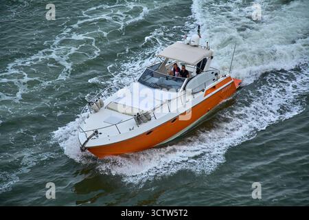 Venedig. Italien - 08. Oktober 2025: Die Motoryacht J-Nation mit markantem orangefarbenen Rumpf fährt mit hoher Geschwindigkeit durch die Gewässer in der Nähe von Venedig. Stockfoto