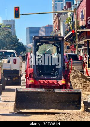 Kleiner Baubagger, der auf einer schmalen Stadtstraße in New Orleans, Louisiana, USA, geparkt ist, mit bunten Gebäuden und Bäumen, die die Straße unter A säumen Stockfoto
