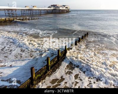 Blick aus der Vogelperspektive auf den Cromer Pier und die brechenden Wellen bei Sonnenaufgang Stockfoto