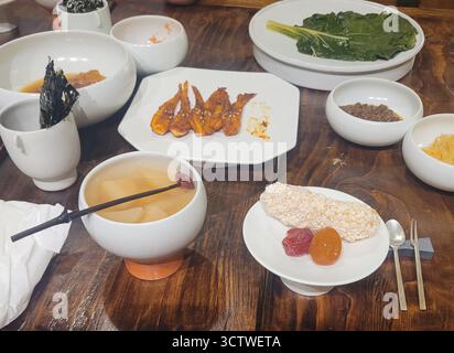 Ein Foto der traditionellen koreanischen Küche in Gyeongju (??), Südkorea, präsentiert mit einer Auswahl an „Banchan“ (??, Beilagen) und Hauptgerichten. Das elegante Aufstrich umfasst einen Snack mit Puffreis, kandierte Früchte, ein traditionelles Getränk wie „Sujeonggwa“ (???), gewürzten Fisch und verschiedene Pasteten und Gemüse. Die koreanische Küche, bekannt als Hansik (??), wird für ihre Betonung auf frische, saisonale Zutaten und die bedeutende Rolle fermentierter Lebensmittel gefeiert. 2025. Stockfoto