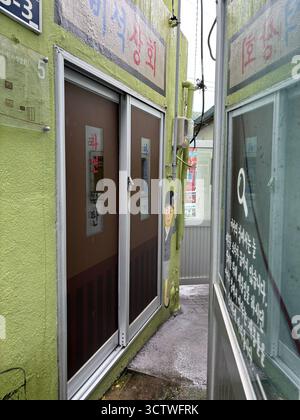 Ein Foto einer engen Gasse im Gamcheon Culture Village im Saha District, Busan, Südkorea. Das Dorf ist bekannt für seine geschichteten Straßen, verwinkelten labyrinthartigen Gassen und hell bemalten Häuser, die in den letzten Jahren restauriert und erweitert wurden, um den Tourismus anzuziehen. Das an einem steilen Berghang errichtete Gamcheon Village wurde in den 1920er und 1930er Jahren gegründet, als die Stadtverwaltung von Busan die Arbeiterbevölkerung umsiedelte. Mitten in der Nachkriegserholung 1955 zogen rund 800 Familien in das Dorf. 2025. Stockfoto