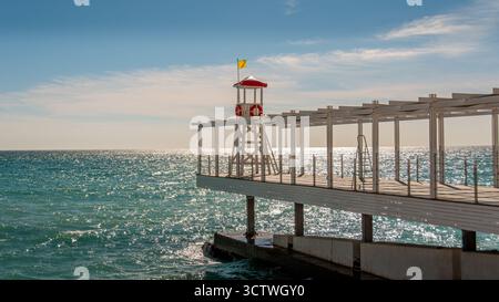 Rettungsschwimmerstuhl am Ende eines Piers über dem Strand in einem Badeort bei Sonnenuntergang. Konzepte der Freizeitreise und des Badeurlaubs. Keine Personen Stockfoto