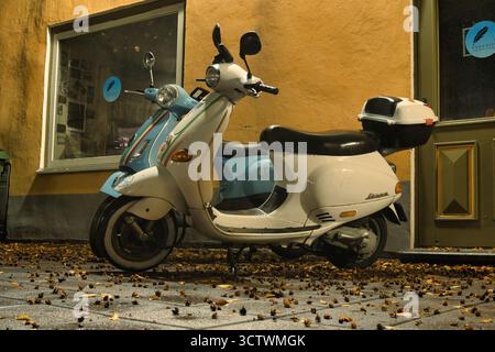 Zwei Vespa-Motorroller parkten auf einer nassen Urban Street mit Herbstlaub Stockfoto