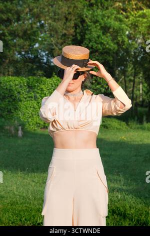 Schöne junge Frau, die einen Retro-Strohhut für einen Sommerspaziergang anzieht Stockfoto