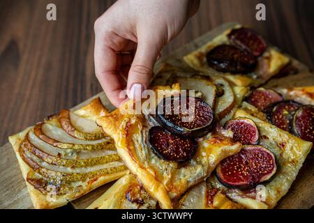 Frisch gebackenes Blättergebäck mit Reifen Feigen und in Scheiben geschnittenen Birnen auf einem Holztisch. Die warmen Farben und goldenen Krusten sorgen für ein gemütliches Herbstgefühl. Stockfoto