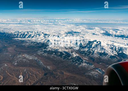 Ein atemberaubender Blick aus der Vogelperspektive auf schneebedeckte Bergketten, teilweise von Wolken verborgen, fotografiert von einem Flugzeugfenster mit einem Teil des Flugzeugengi Stockfoto