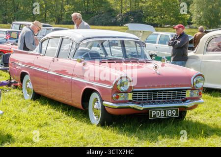 Klassischer, rosa-weißer vauxhall cresta-Oldtimer, der auf einer Autoshow auf einem grasbewachsenen Feld ausgestellt wird und die Leute Fahrzeuge im Hintergrund bewundern Stockfoto