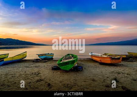 Farbenfrohe Fischerboote ruhen bei Sonnenuntergang am Sandufer des Lake Ohrid mit ruhigem Wasser und weit entfernten Bergen in Pogradec, Albanien Stockfoto