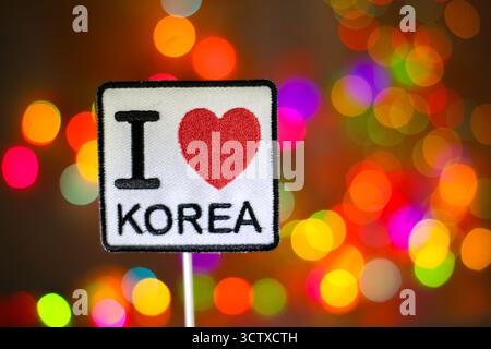 Ich LIEBE KOREA Patch auf einem Regenbogen-Bokeh-Hintergrund. Farbenfrohe, verschwommene Lichter schaffen eine festliche Atmosphäre, ideal für Korea-Reisen und Neujahrsthemen. Stockfoto