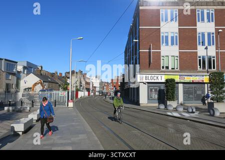 Dublin, Irland - 08. Juni 2015 - die Luas-Straßenbahnlinie in Smithfield an einem sonnigen Nachmittag, während ein Mann in Dublin vorbeifährt und das Straßenleben in der irischen Hauptstadt schildert Stockfoto