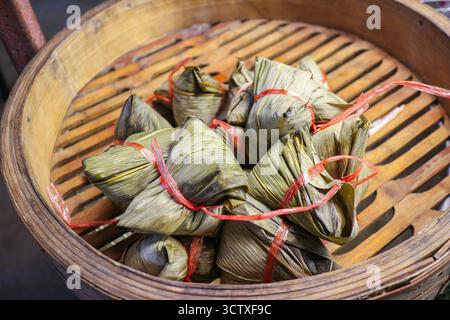 Klebrige Reisknödel (Bajang), in Blätter gewickelt, in einem Bambusdampfer ausgestellt. Klassische thailändische/chinesische Street Food-Tradition. Stockfoto