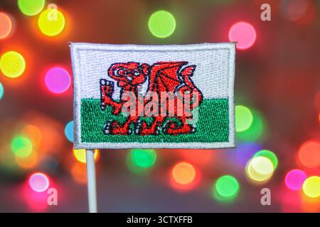 Nahaufnahme einer detailreich gestickten walisischen Flagge vor einem mehrfarbigen, weichen Bokeh, ideal für Weihnachten und Neujahr. Stockfoto