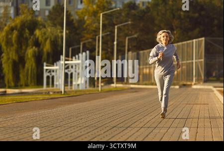 Aktive Seniorin joggt draußen im Park und trägt Sportswear am sonnigen Morgen Stockfoto