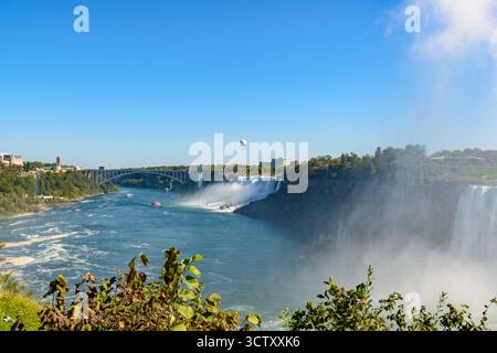 Ein pulsierender Panoramablick auf die American Falls bei den Niagara Falls, New York, mit der berühmten Rainbow Bridge, die die USA und Kanada in der verbindet Stockfoto