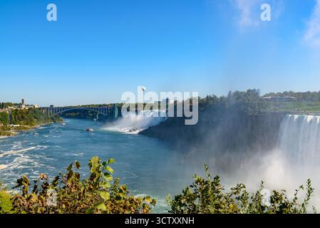 Ein pulsierender Panoramablick auf die American Falls bei den Niagara Falls, New York, mit der berühmten Rainbow Bridge, die die USA und Kanada in der verbindet Stockfoto