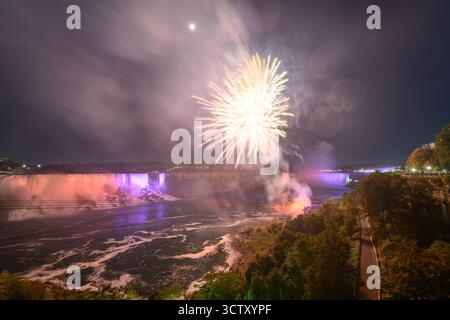 Ein spektakulärer Blick bei Nacht auf die Niagarafälle mit den kanadischen Horseshoe Falls und den American Falls, beleuchtet von einem lebhaften Feuerwerk. Stockfoto