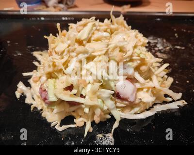 Traditionelles japanisches Okonomiyaki, das auf einem Teppan-Grill zubereitet wird, mit köstlicher Textur und authentischem Street Food-Stil. Stockfoto
