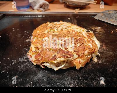 Traditionelles japanisches Okonomiyaki, das auf einem Teppan-Grill zubereitet wird, mit köstlicher Textur und authentischem Street Food-Stil. Stockfoto