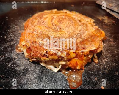 Traditionelles japanisches Okonomiyaki, das auf einem Teppan-Grill zubereitet wird, mit köstlicher Textur und authentischem Street Food-Stil. Stockfoto