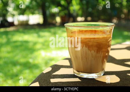 Ein Glas schmutzigen Latte-Kaffee wird auf dem Gartentisch serviert Stockfoto