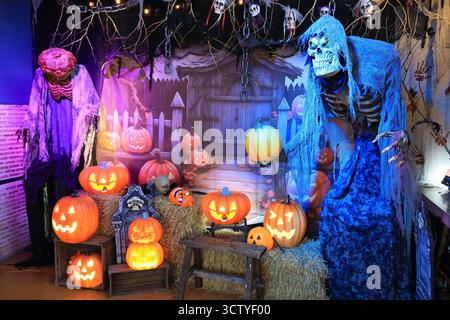 Gruselige Halloween-Dekoration mit einem Haufen von Jack-O'-Laternen Kürbis-Laternen und beleuchtetem Skelett im Garten Stockfoto