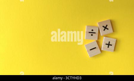 Grundlegende arithmetische Operationssymbole auf verstreuten Holzblöcken vor leuchtendem gelbem Hintergrund mit Kopierraum. Stockfoto