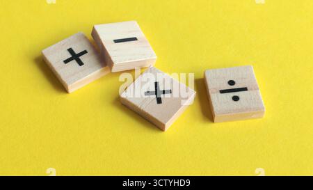 Verstreute Holzblöcke mit grundlegenden mathematischen Symbolen auf hellgelbem Hintergrund, die Bildung, Wachstum und finanzielle Entscheidungen darstellen. Stockfoto