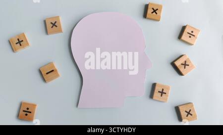 Menschliche Kopf-Silhouette umgeben von verstreuten hölzernen Mathesymbolen, die komplexe Berechnungen, pädagogische Herausforderungen und tiefgreifende analytische du repräsentieren Stockfoto