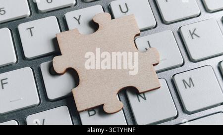 Einzelnes Puzzleteil aus Holz, das auf einer modernen weißen Computertastatur aufliegt und digitale Lösungen, Online-Problemlösung und Technologie i symbolisiert Stockfoto