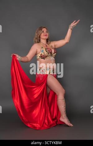 Kurvige Barfuß-Tänzerin in voller Länge vor grauem Hintergrund. Erwachsene Kaukasierin mittleren Alters kleidet sich in Tanzkostüm - BH-Top und Stockfoto