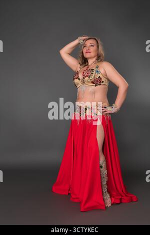 Inspirierendes Models und Bauchtänzerin mit Hand im Haar, gekleidet in Tanz-Outfit - Bralette und roter langer Rock mit Schlitz barfuß stehend Stockfoto