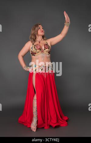 Authentische Bauchtänzerin mittleren Alters und Modemodell mit Tanzkostüm – BH-Oberteil und langer, scharlachrote Rock mit Schlitz lässt sich barfuß nach innen bewegen Stockfoto
