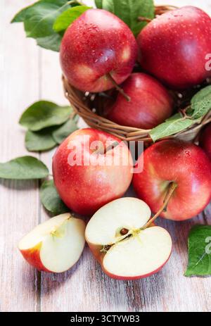 Geerntete rote Äpfel in einem gewebten Korb mit geschnittenen Früchten auf hellem hölzernem Hintergrund Stockfoto