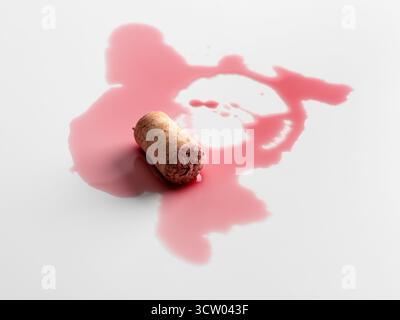 Rotweinkork mit verschütteter Flüssigkeit, die abstrakten Flecken auf hellem Hintergrund erzeugt. Unfallbegriff, Unvollkommenheit und symbolische Eleganz im Minimalismus Stockfoto