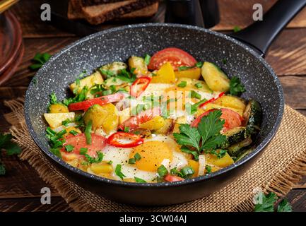 Spiegeleier und Kartoffeln, Tomaten, Zucchini und Chili auf Holztisch. Stockfoto