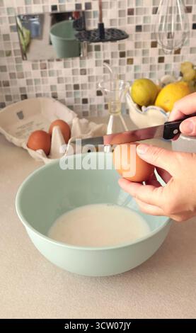 Eine anonyme Person bereitet den Teig in einer Schüssel zu und knackt mit einem Messer ein Ei. Gesunde Ernährung mit biologischen, glutenfreien Zutaten. Hausmannskost. Stockfoto