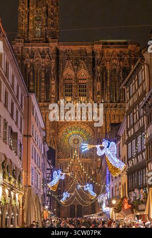 STRASSBURG, FRANKREICH – 12. DEZEMBER 2024: Die beleuchtete Kathedrale Notre-Dame von Straßburg steht majestätisch hinter einem geschäftigen Weihnachtsmarkt Stockfoto