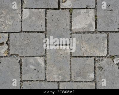 Grauer Natursteinpflaster mit blockgebundenen Fugen, Rissen und Moos. Eine detaillierte Fläche. Ideal als Textur. Kopierraum Stockfoto